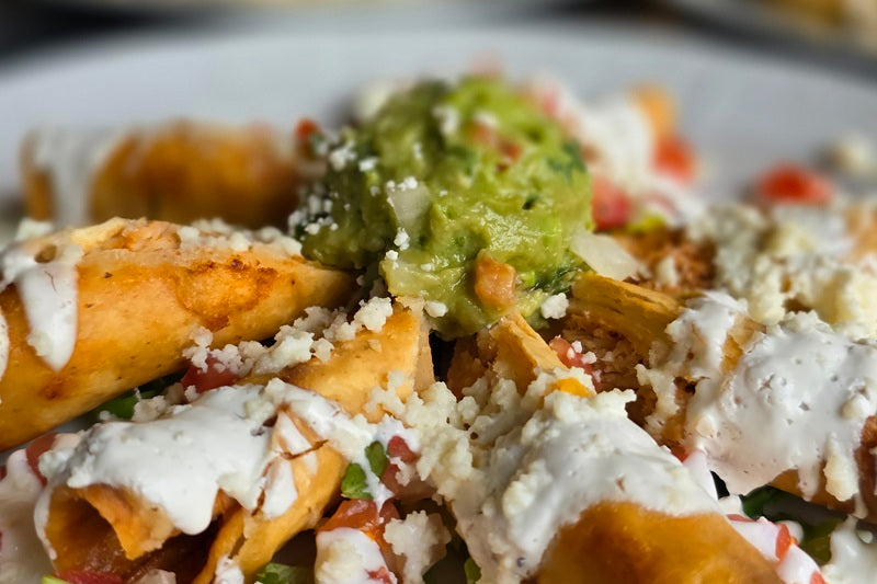 Rolled tortillas filled with meat and fried covered in sour cream and guacamole sprinkled with cheese