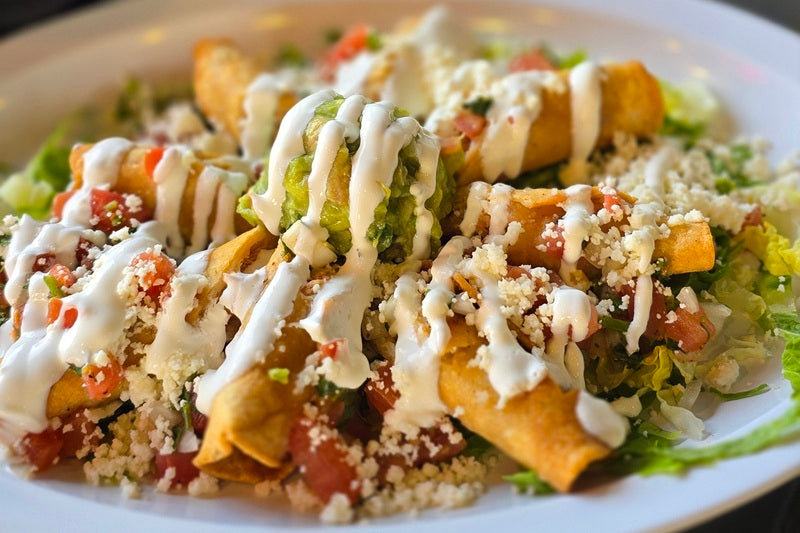 A Plate of Flautas Sprinkled with Cheese, Drizzled with Sour Cream, and Topped with a Dollop of Guacamole