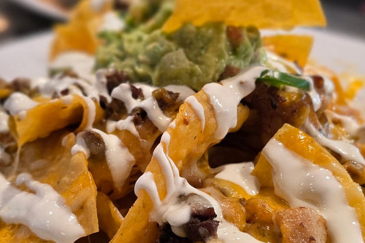 Close Up of Nachos with Cheese, Sour Cream, and Guacamole on a White Plate
