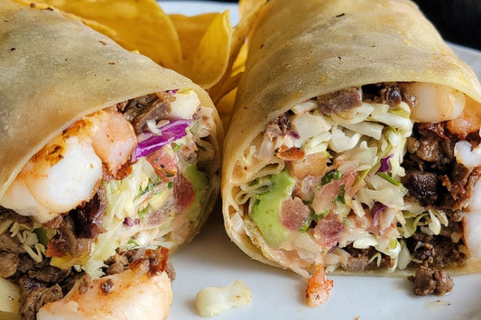 A shrimp burrito cut in half exposing the shrimp, beef, lettuce, sauce on a white plate