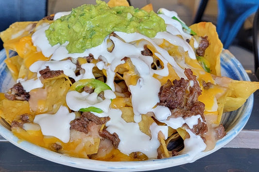Close Up of a Plate of Nachos Consisting of Tortilla Chips Topped with Meat, Cheese Sauce, Sour Cream and Guacamole