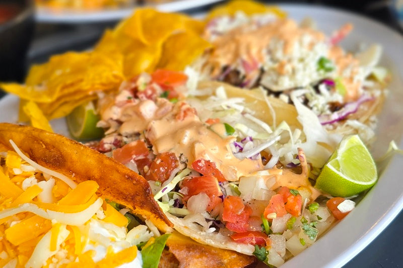 A Plate of Tacos Topped with Shredded Lettuce, Sauce, Pico de Gallo, and a Lime Wedge on a White Plate