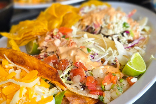 A Plate of Tacos Topped with Shredded Lettuce, Sauce, Pico de Gallo, and a Lime Wedge on a White Plate