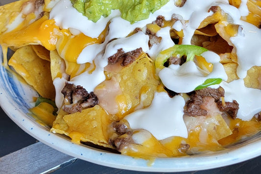 Tortilla Chips Covered in Melted Cheese Topped with Meat and Jalapenos, Drizzled with Sour Cream and a Dollop of Guacamole On Top