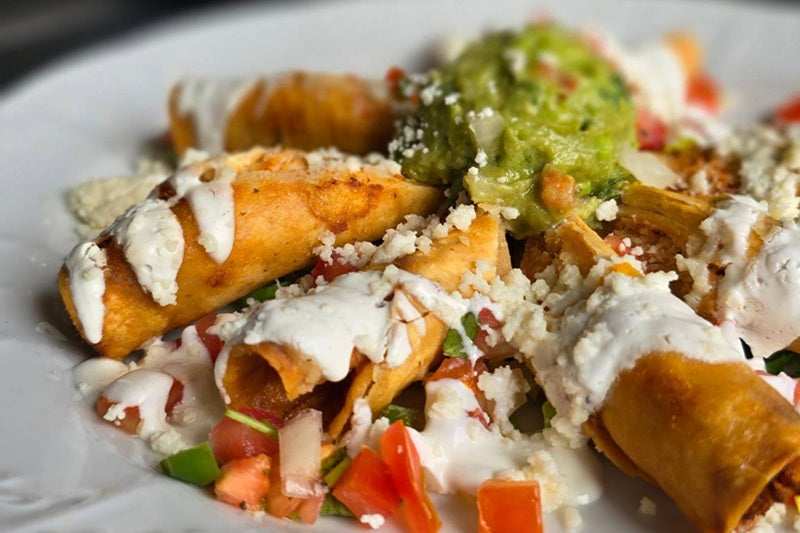 A Plate of Flautas Drizzled with Sour Cream, Topped with Guacamole, and Sprinkled with Cheese