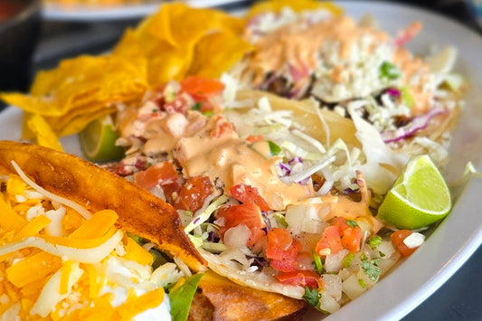 Three Tacos on a Plate Filled with Meat, Cheese, and Salsa with a Lime Wedge on a White Plate