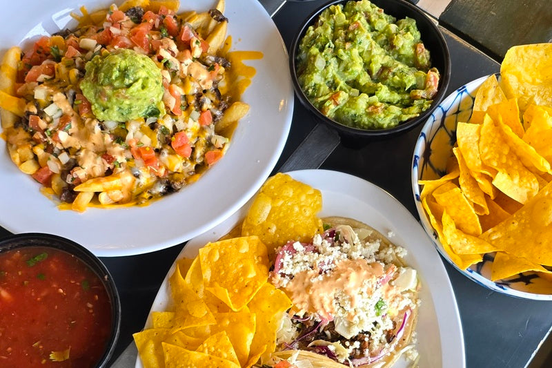 A bowl of guacamole/ a bowl of salsa/ a plate of carne asada fries topped with cheese, meat, guac, and salsa/ a plate of tacos with meat and cheese, with tortilla chips/ a bowl of tortilla chips