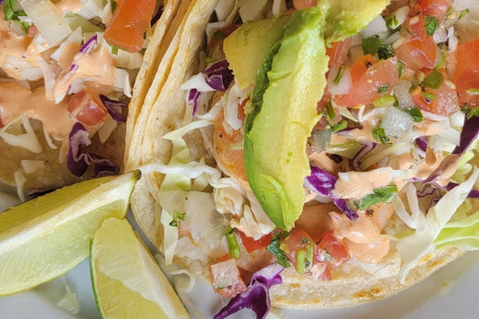 Close Up of Tacos with Shredded Lettuce, Sauce, Avocados, and Pico de Gallo with Two Lime Wedges on the Plate